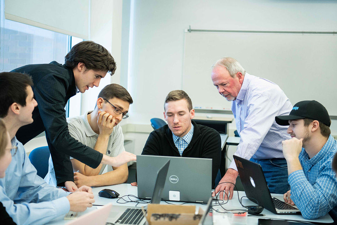 students and researcher crowding around laptop computer.