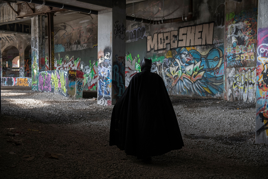 a person dressed as Batman facing a wall of graffiti. 