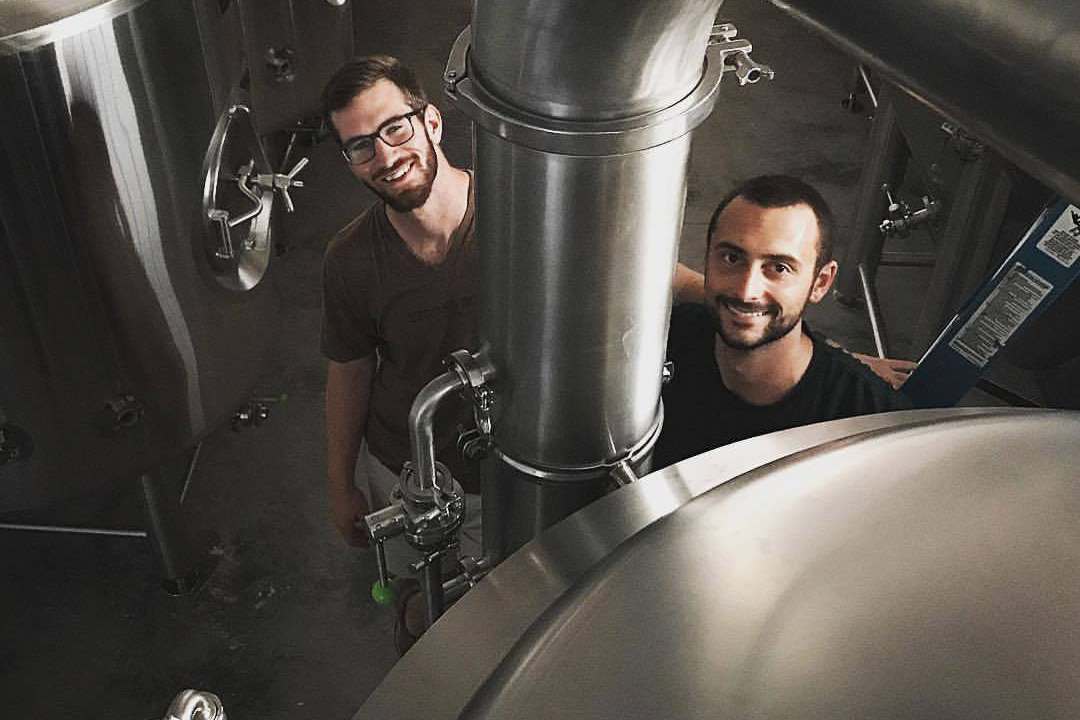 two people standing near vat of beer.