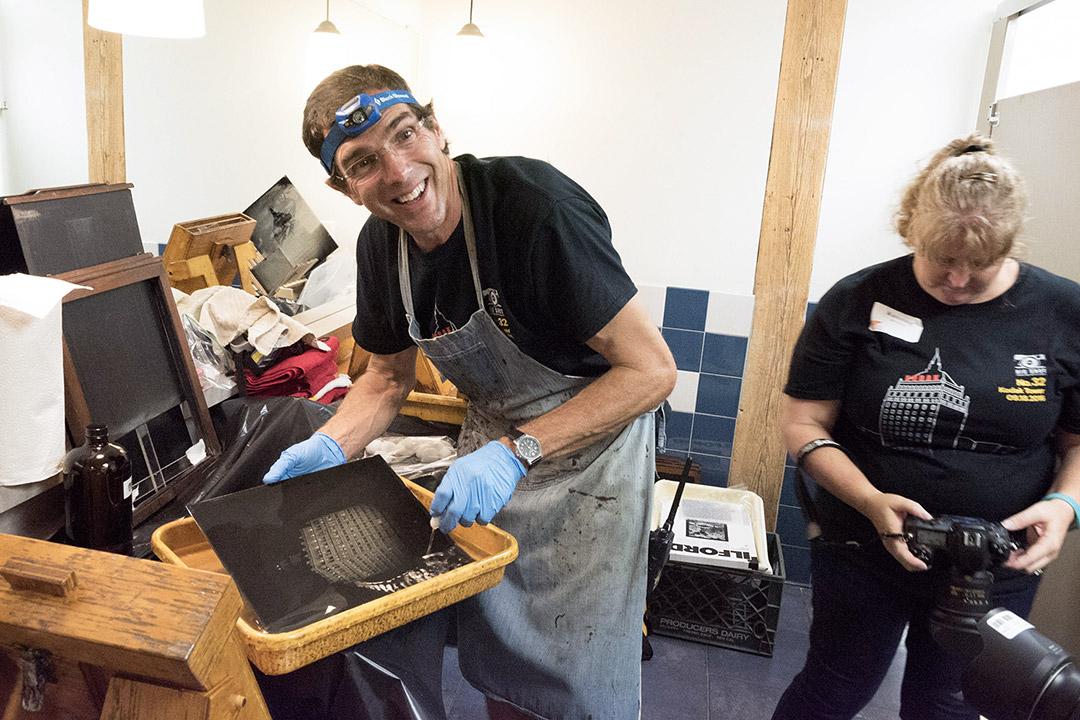 photographer wearing a head lamp and an apron developing a photo in a men's bathroom.