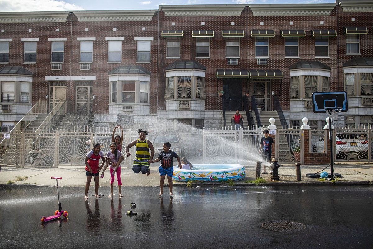 People hang out in the streets of New York City as they're showered by an opened fire hydrant
