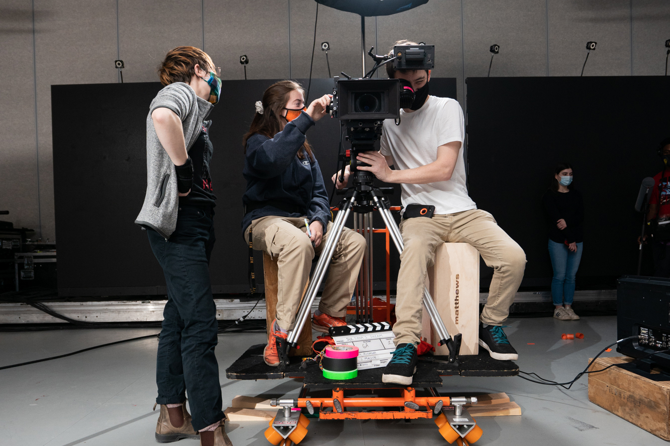 Two students and an alumnus operate a camera together.