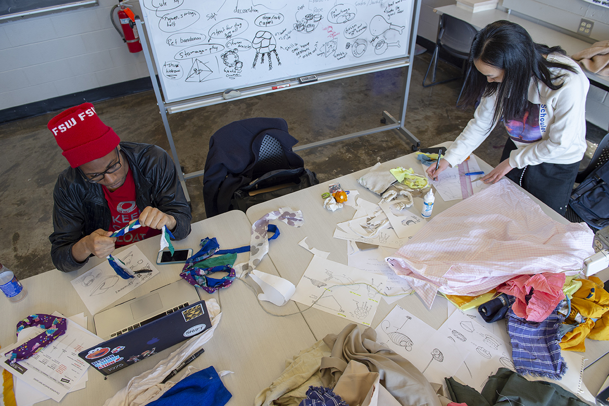 Two students at a table sketching and using fabric to make a product. 