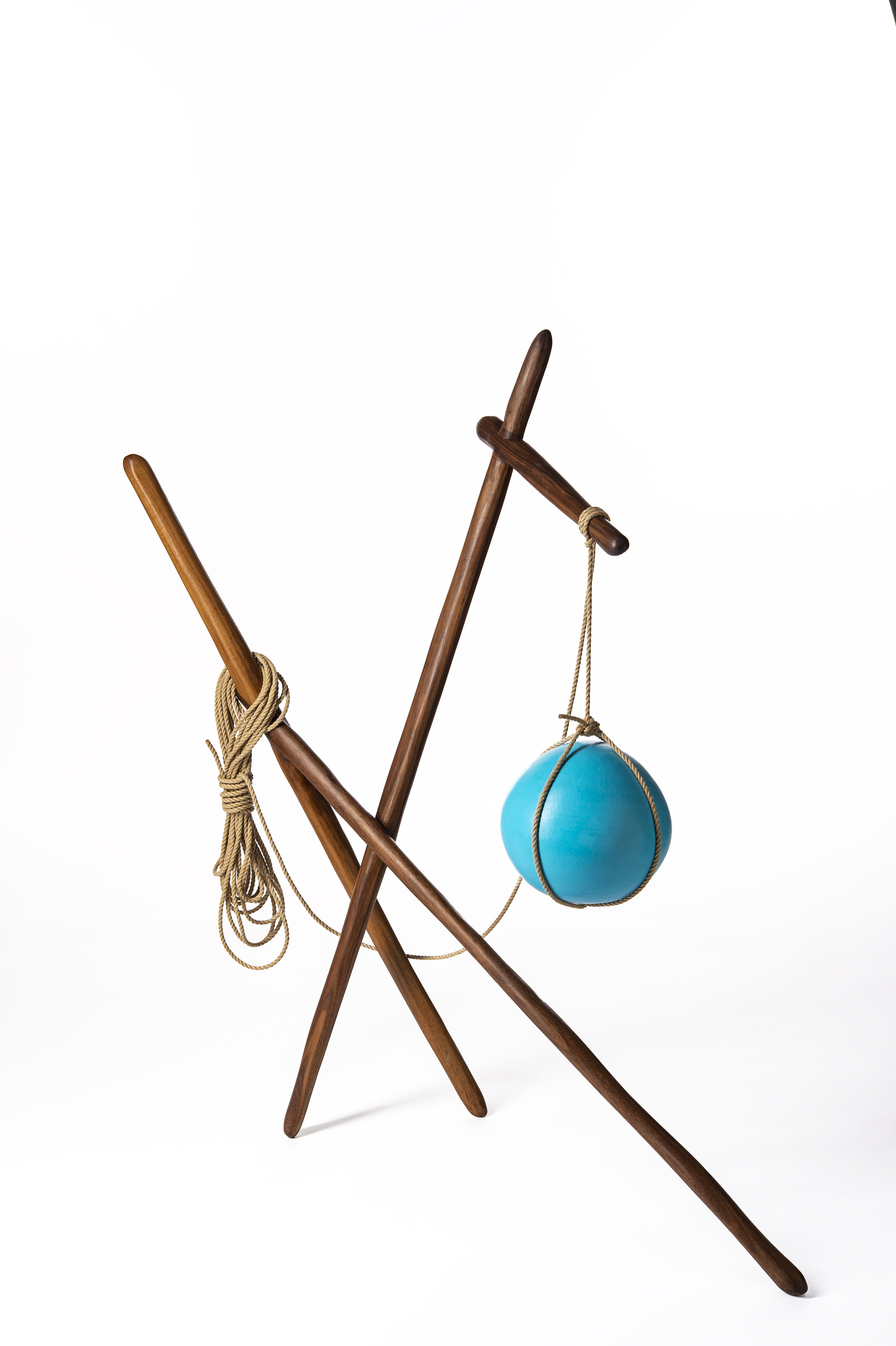 A wood sculpture with a rope holding a blue ball.