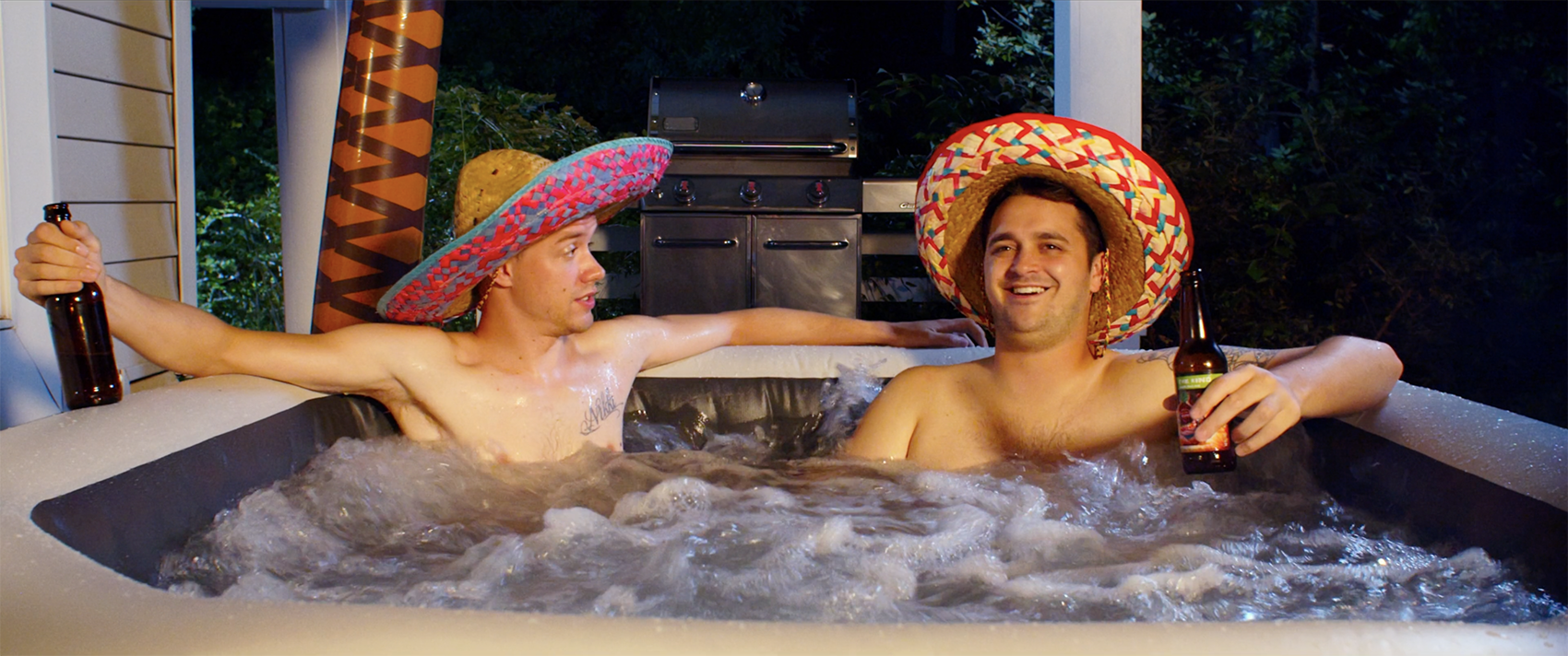 Two guys wearing sombreros sit in a hot tub.