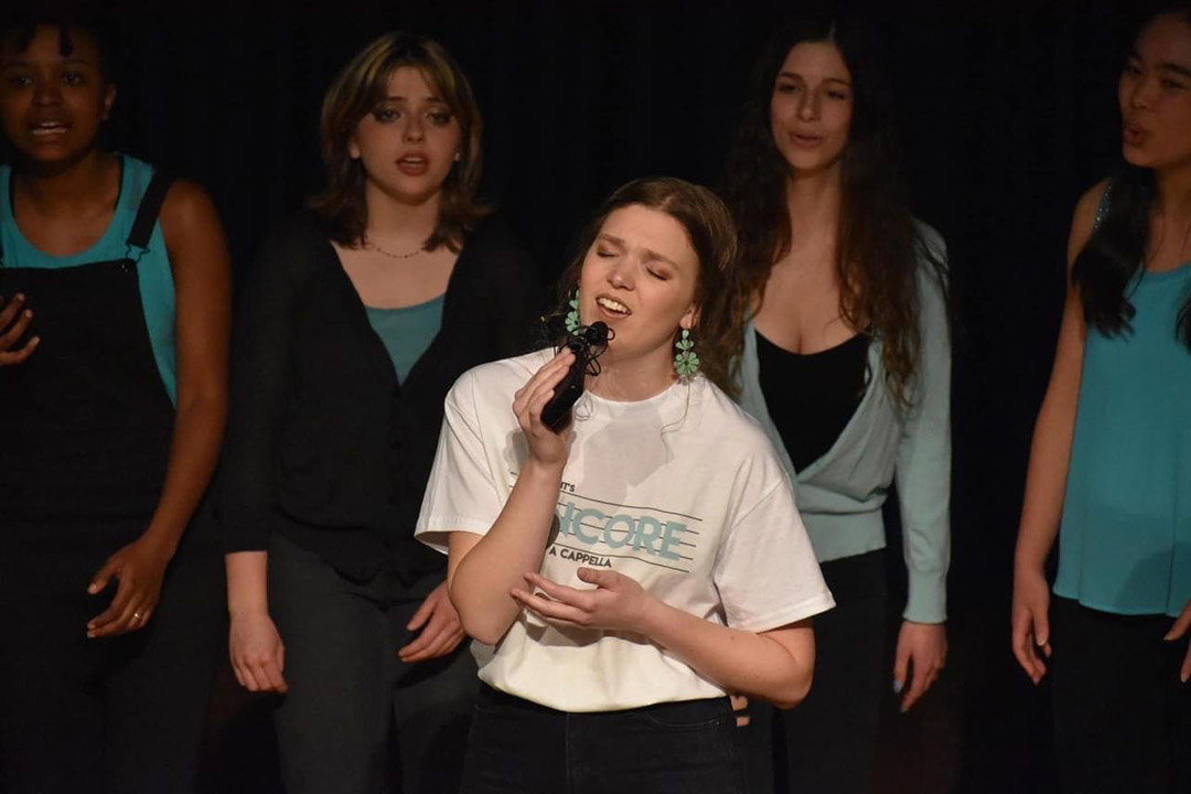 college student singing with four back-up singers behind her.