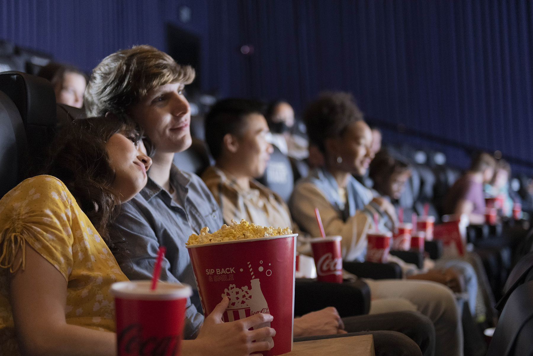 Two people share popcorn and Cokes in the movie theater.