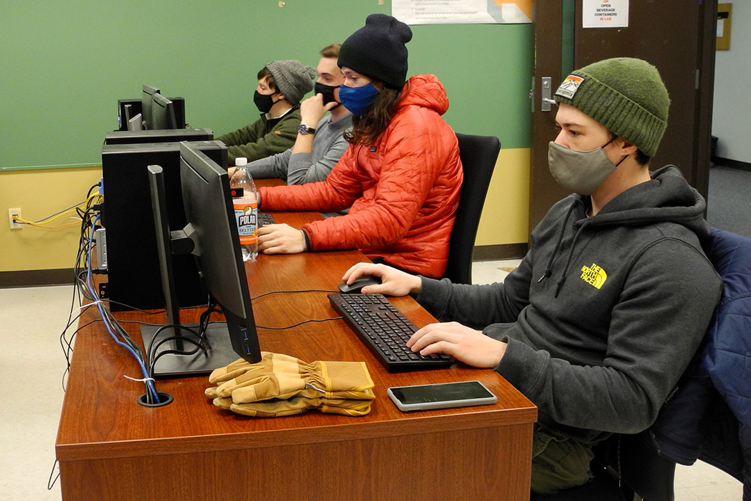 four students sitting at a table working on computers.