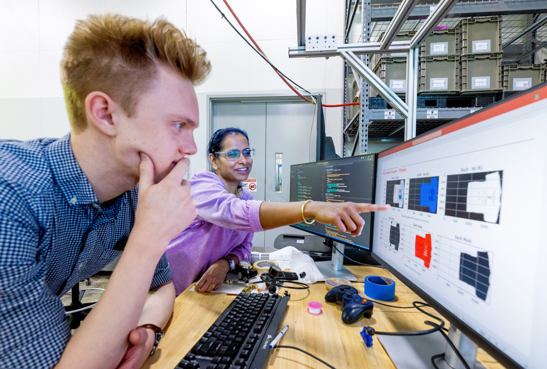 A professor points at a computer screen as a student looks on