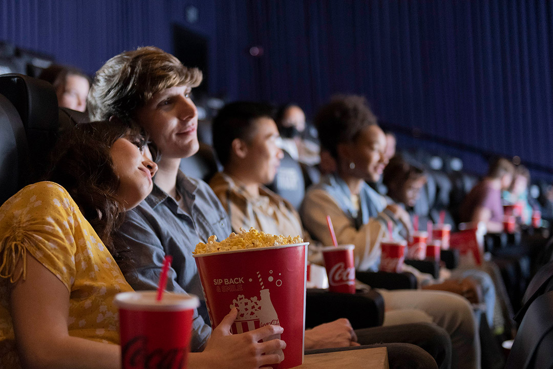 people in a movie theater eating popcorn and drinking Coca-Cola.