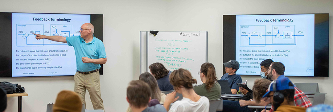 a professor pointing to a smart board in front of a class on feedback terminology for college students.