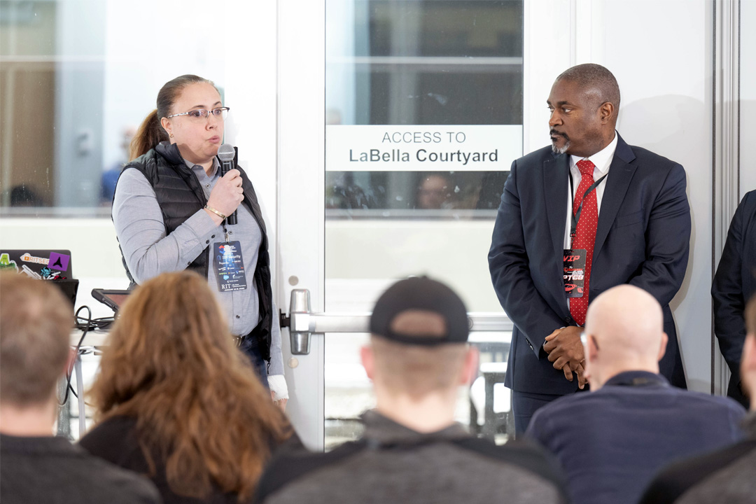 Woman and man speak with microphones in front of audience.