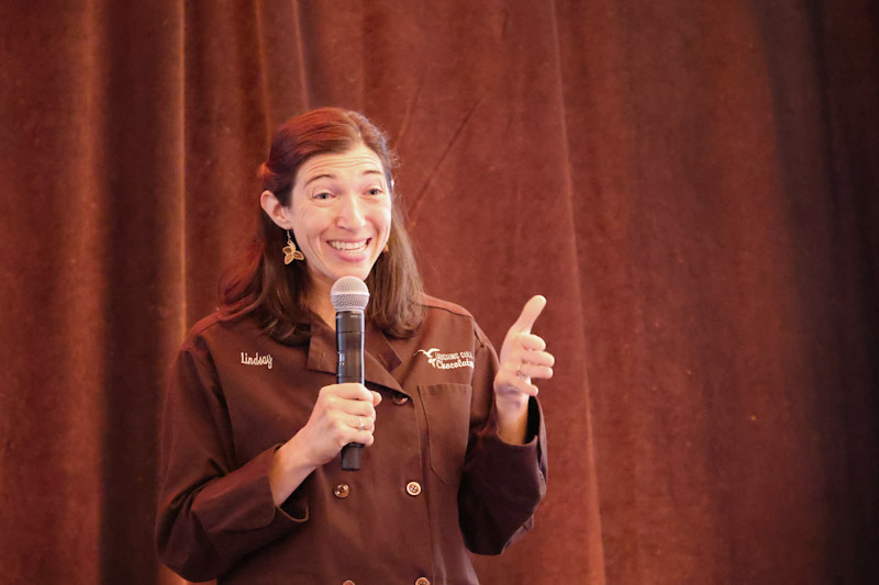 A brown chef wearing a coat and holding a microphone while giving a speech