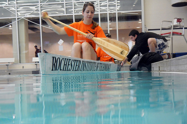 Student floats in concrete canoe in pool.