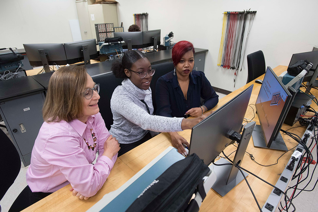 Professor working with two students on computer.