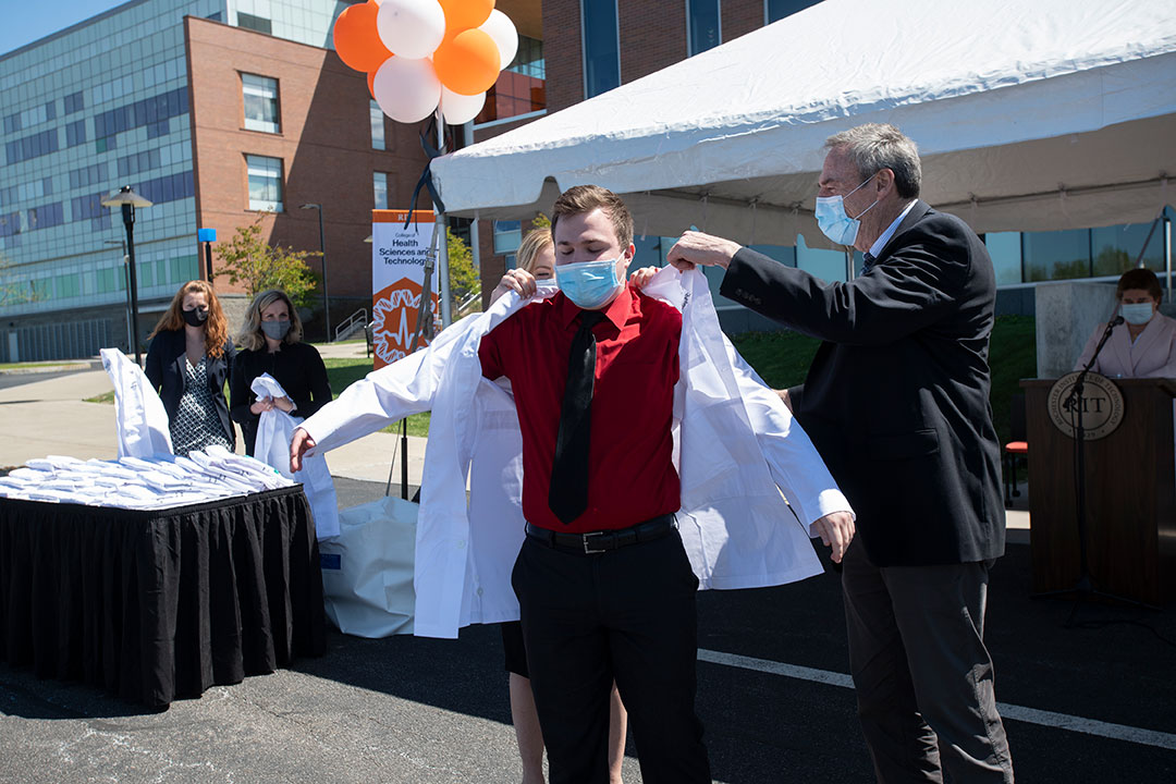 professor puts white lab coat on student.