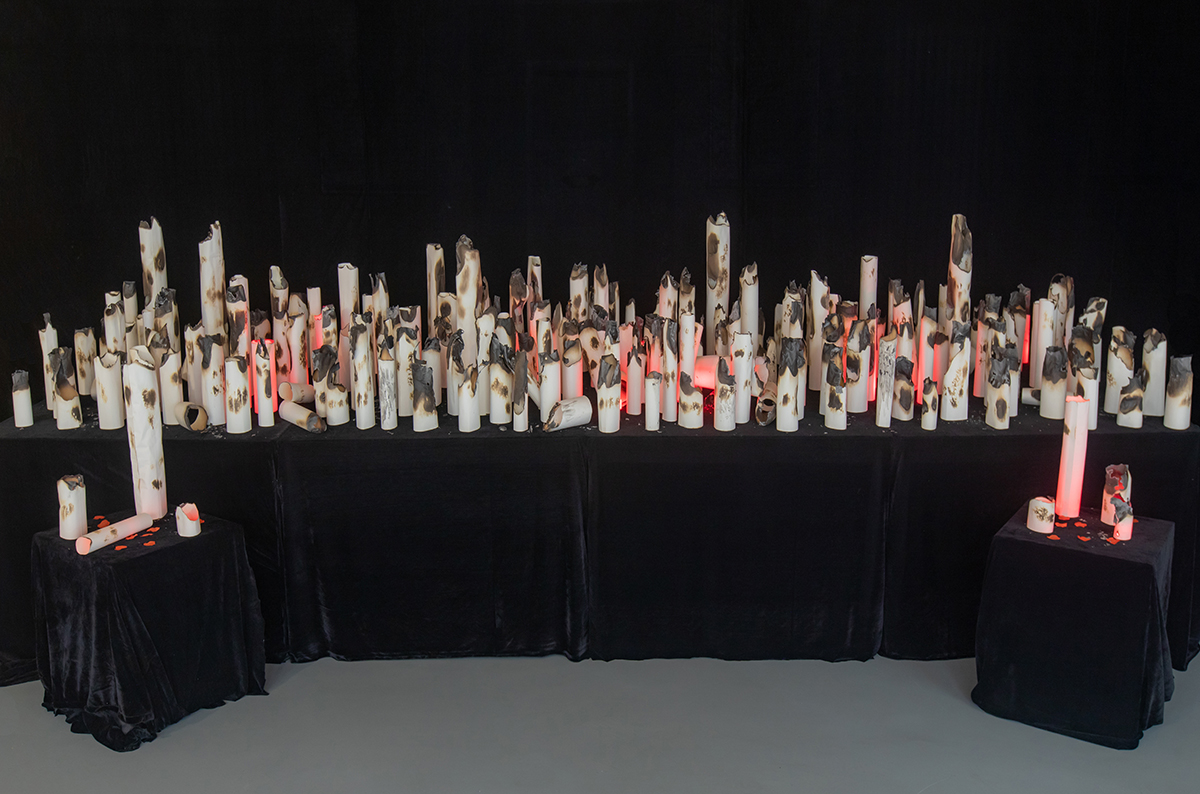 Dozens of cylinder-shaped pieces of paper lit by LED light sit close together on tables.