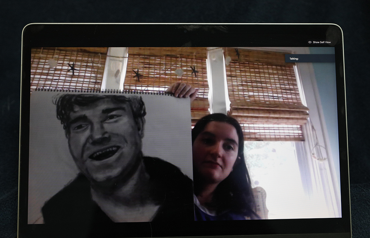 A student holds up a portrait she drew for a workshop assignment.