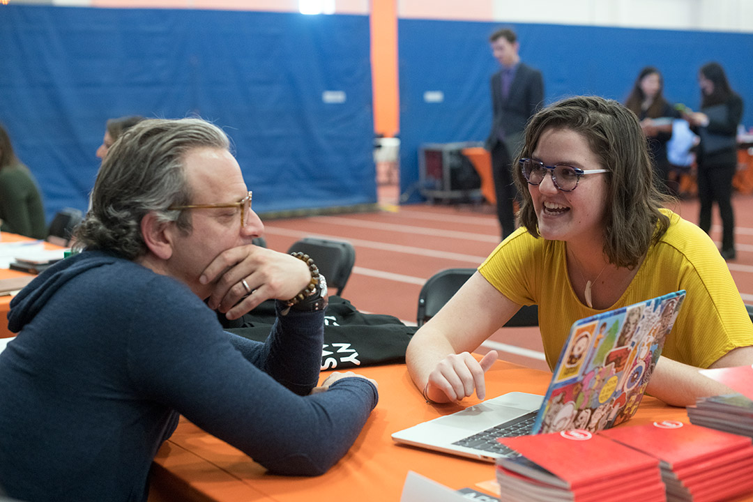 student shows artwork to company rep at career fair.