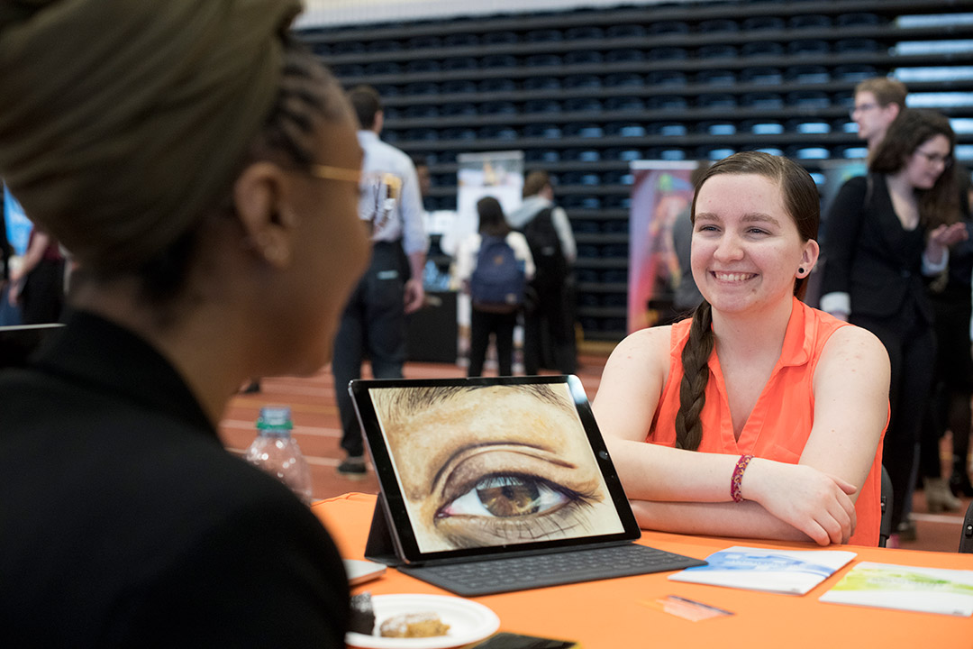 student smiling as she shows graphic illustration of an eye to a company rep.