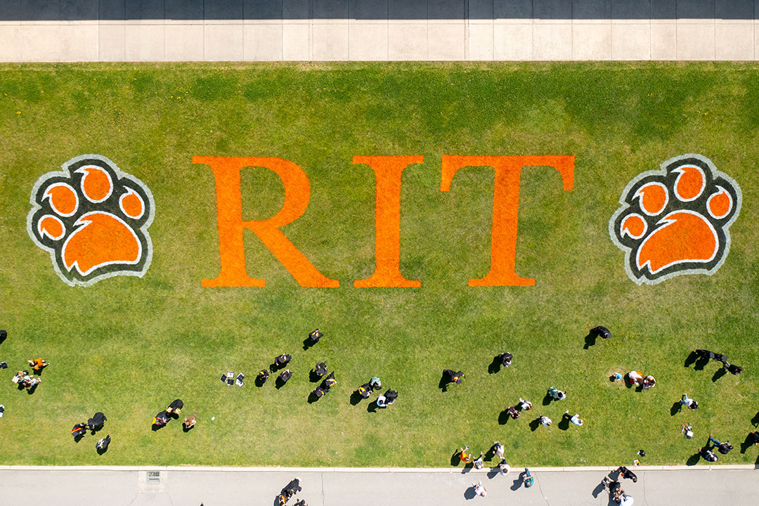 overhead view of students walking on field spray painted with the RIT logo.