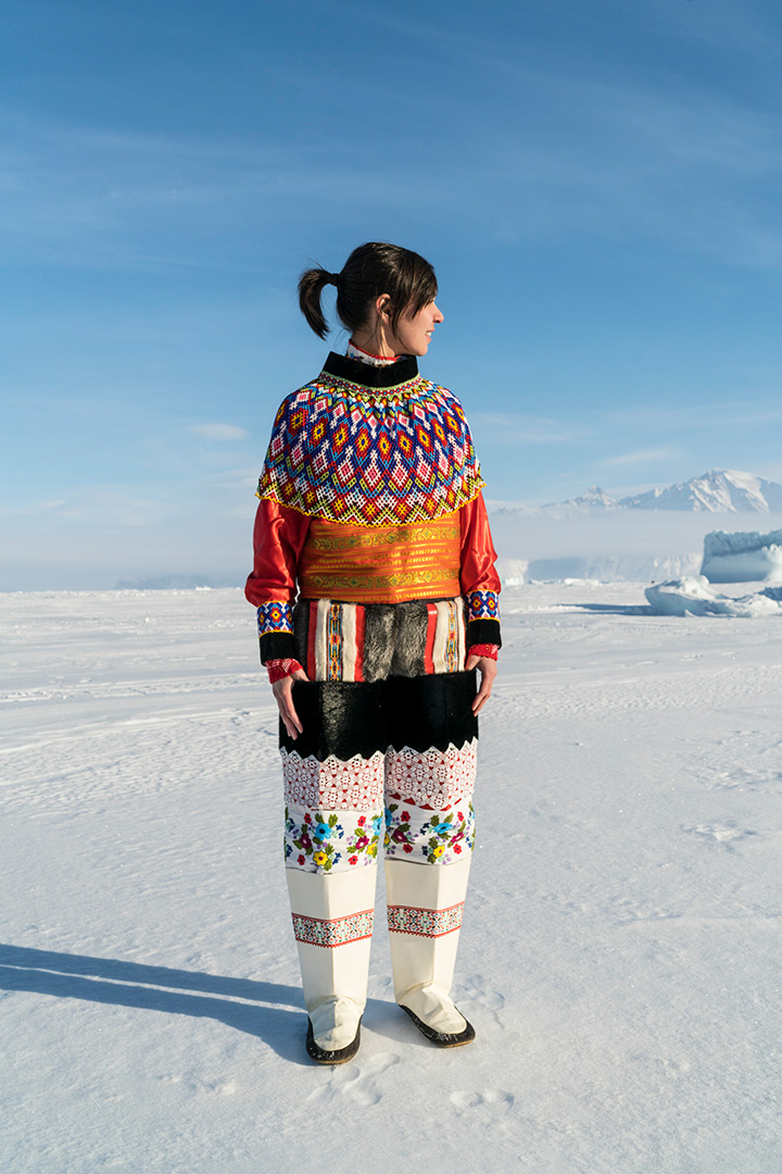 A woman stands in a snow covered landscape wearing traditional Greenlandic clothing