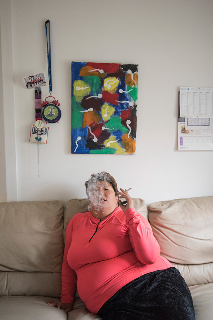 A woman sits on a couch and smokes a cigarette