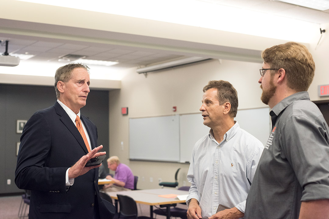 Three men speak to each other in classroom.