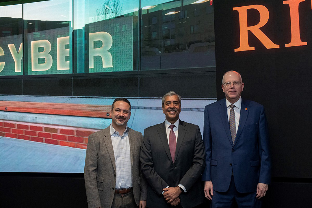 three men standing in front of a screen showing an image of a building.