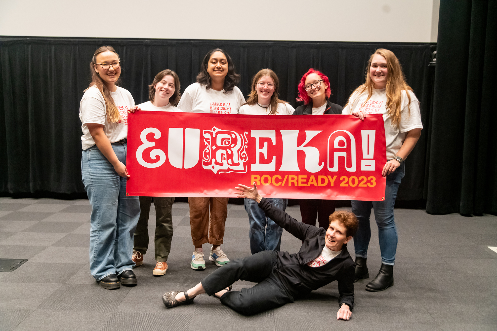 A group of students and faculty hold up a EUREKA! 2023 banner.
