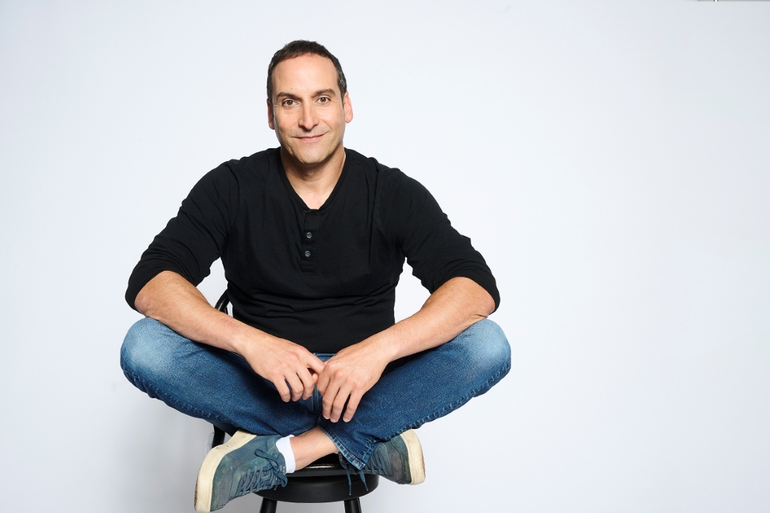 a man in a black long sleeve shirt and jeans sits against a white background
