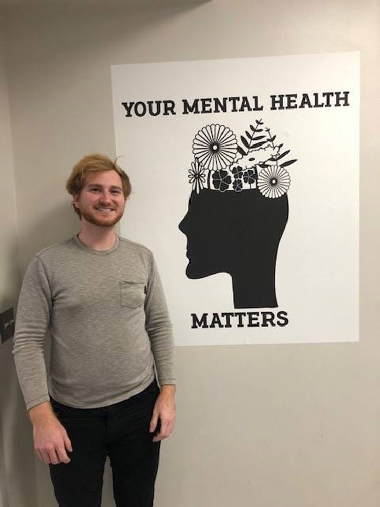 college student standing next to a poster that reads, your mental health matters.