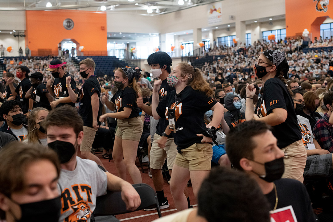 Orientation leaders dance in an aisle between seated students.