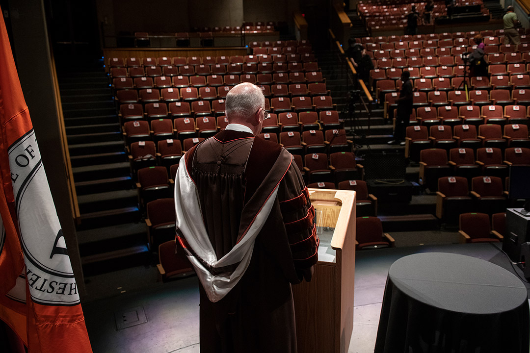 President Munson delivering speech in front of empty auditorium.