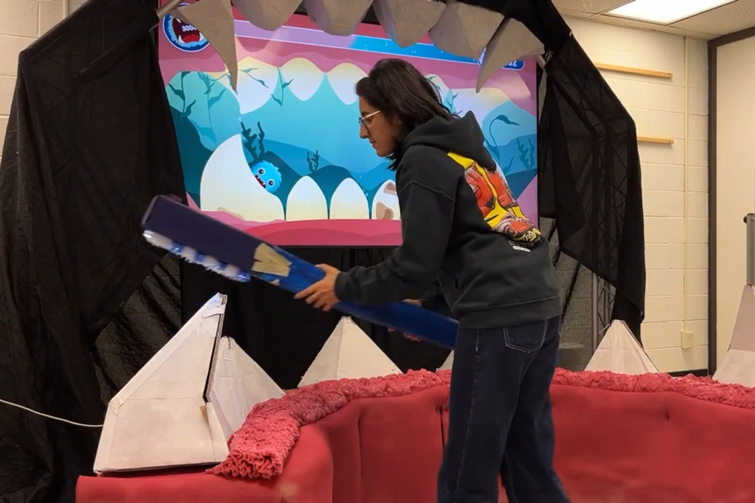 A student uses a giant toothbrush in front of an interactive game screen.