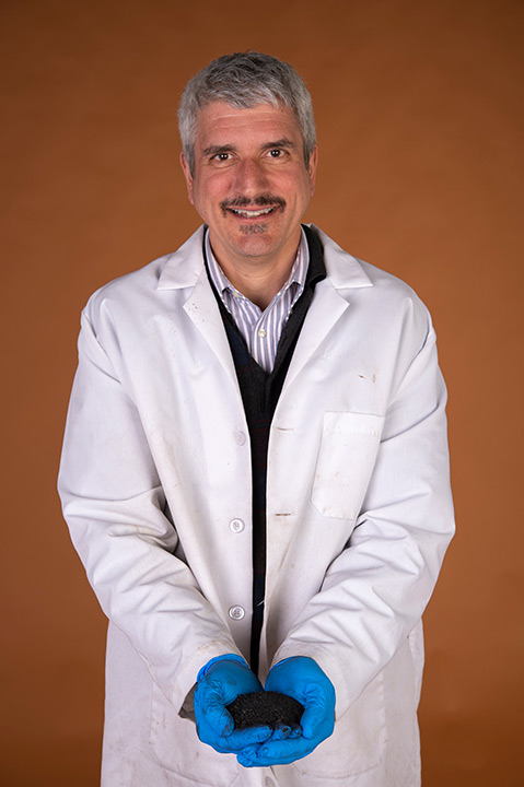 Man in lab coat holds pile of dirt.