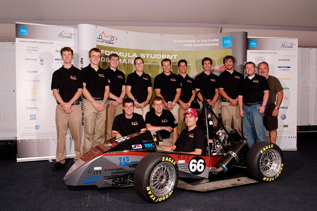 team of 13 students and professor standing around their Formula race car.