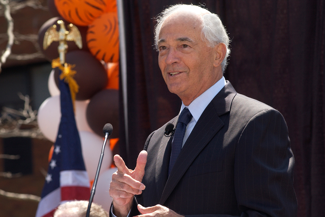 man speaking at podium outdoors.