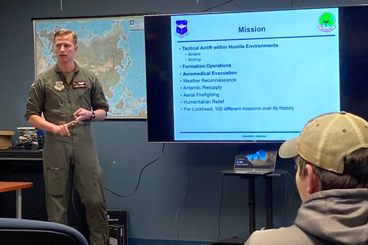 Air Force captain giving a presentation next to a slide about the Air Force mission.
