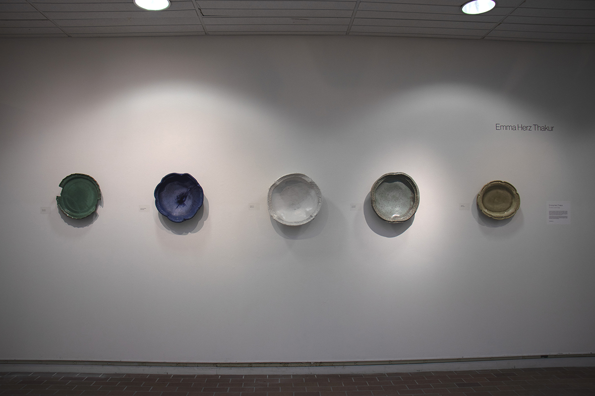 Five ceramic plates hang on a gallery wall.