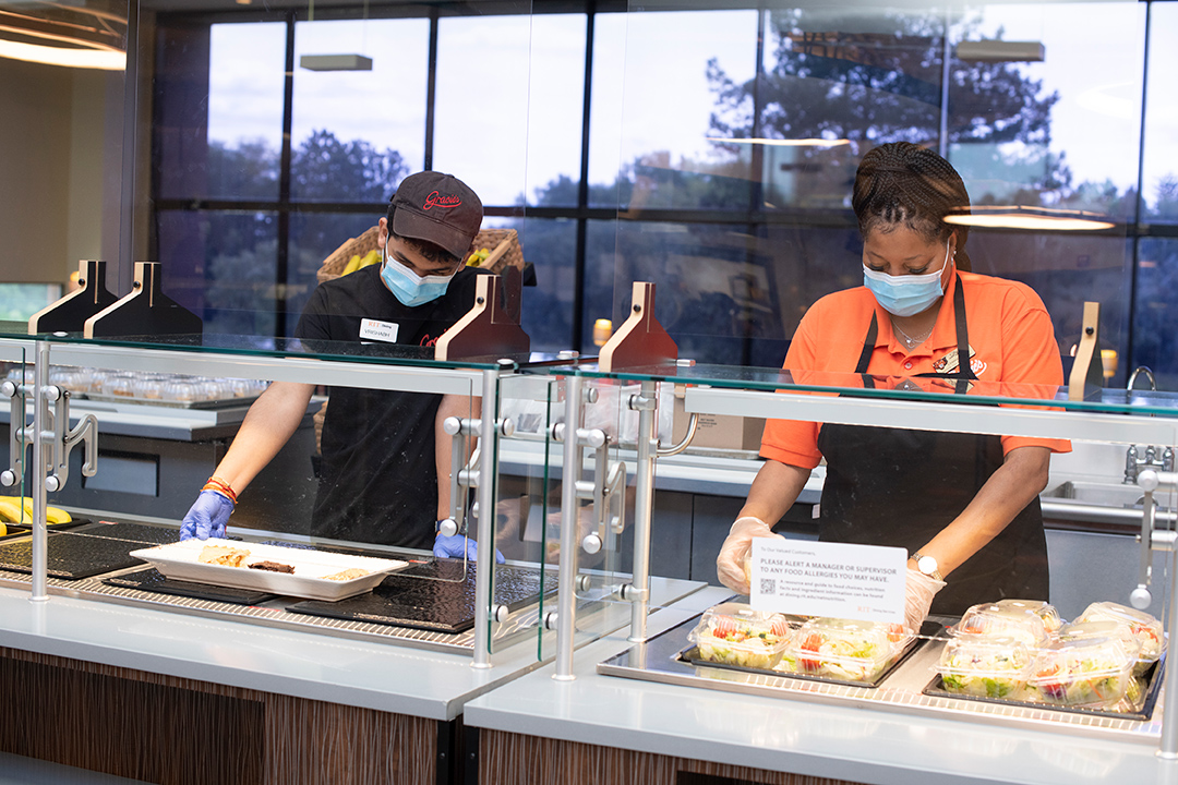 two food workers prepare a meal in a cafeteria.