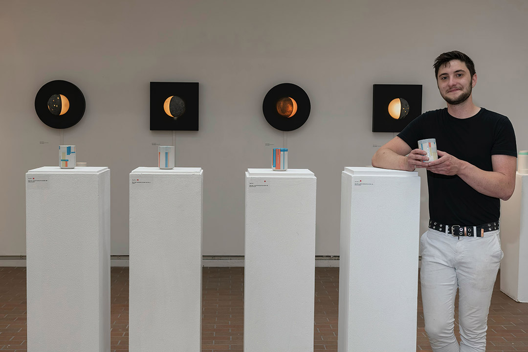 artist standing next to four pillars, each topped with a ceramic piece.
