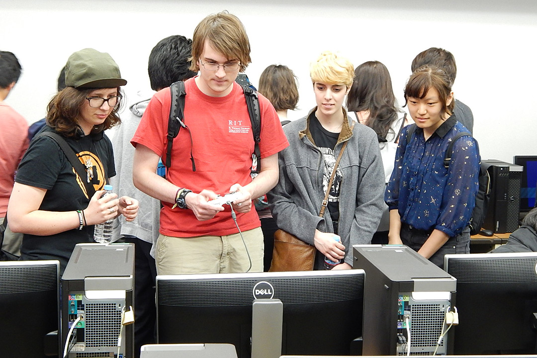 students standing playing a game on a computer.