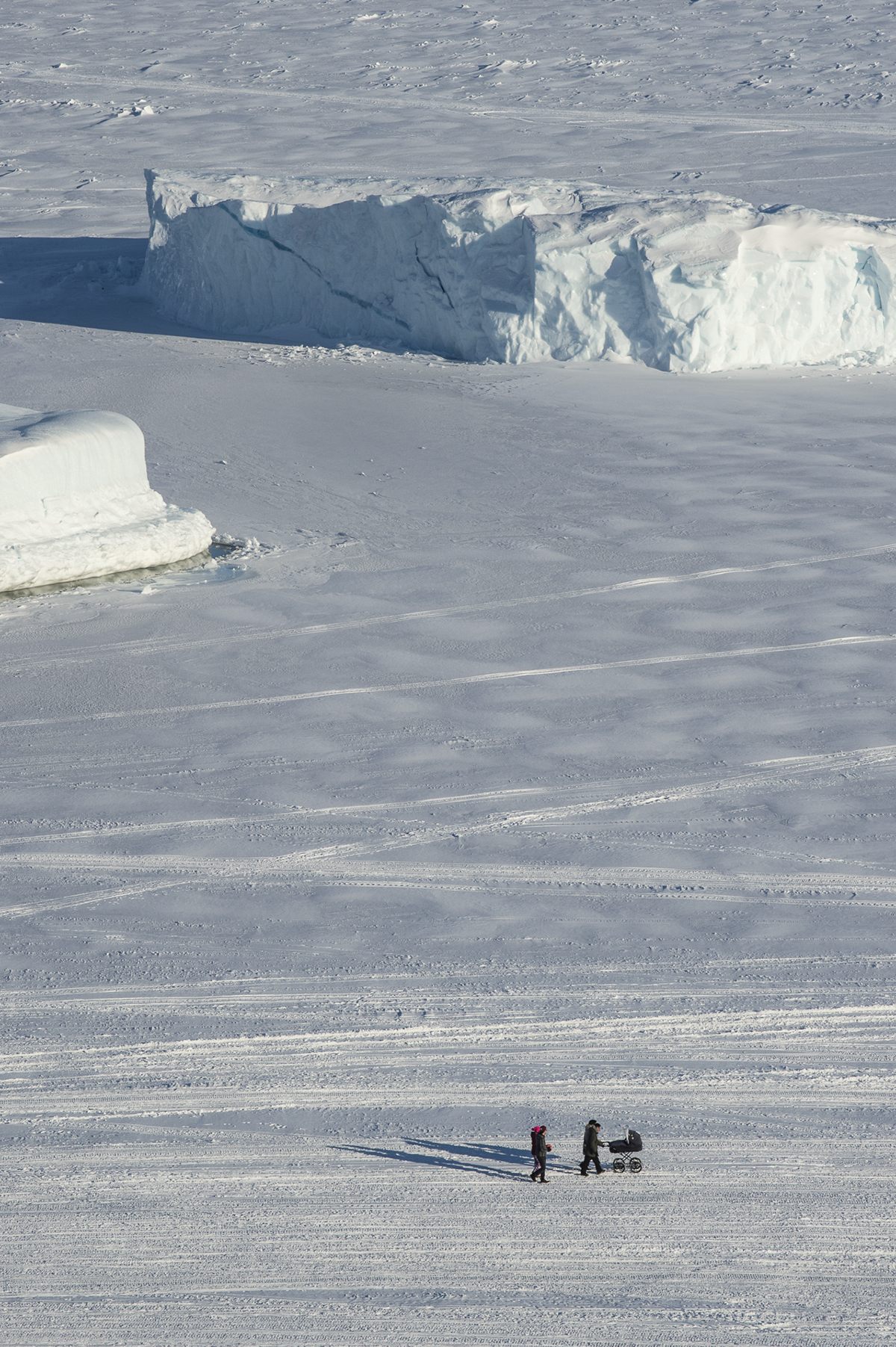 A family, with a baby in a carriage, walks on a snowy, sunny day in Greenland. The photo was taken as part of Denis Defibaugh's NSF grant.