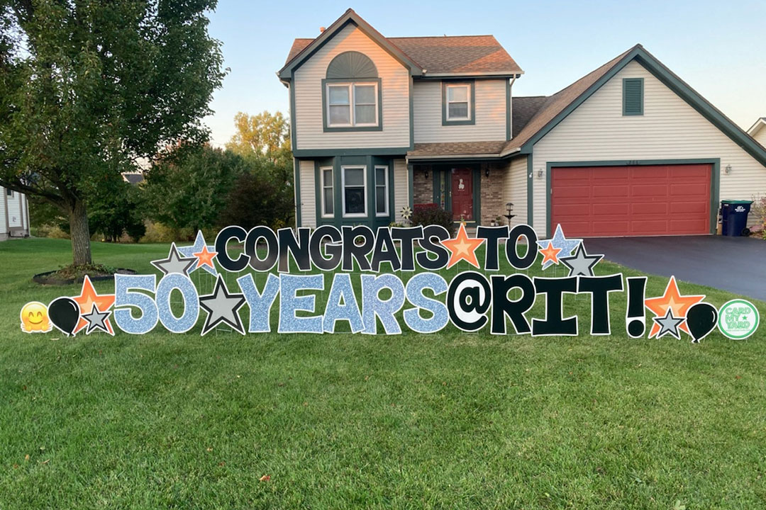 large lawn sign in front of house that reads: congrats to 50 years at RIT.