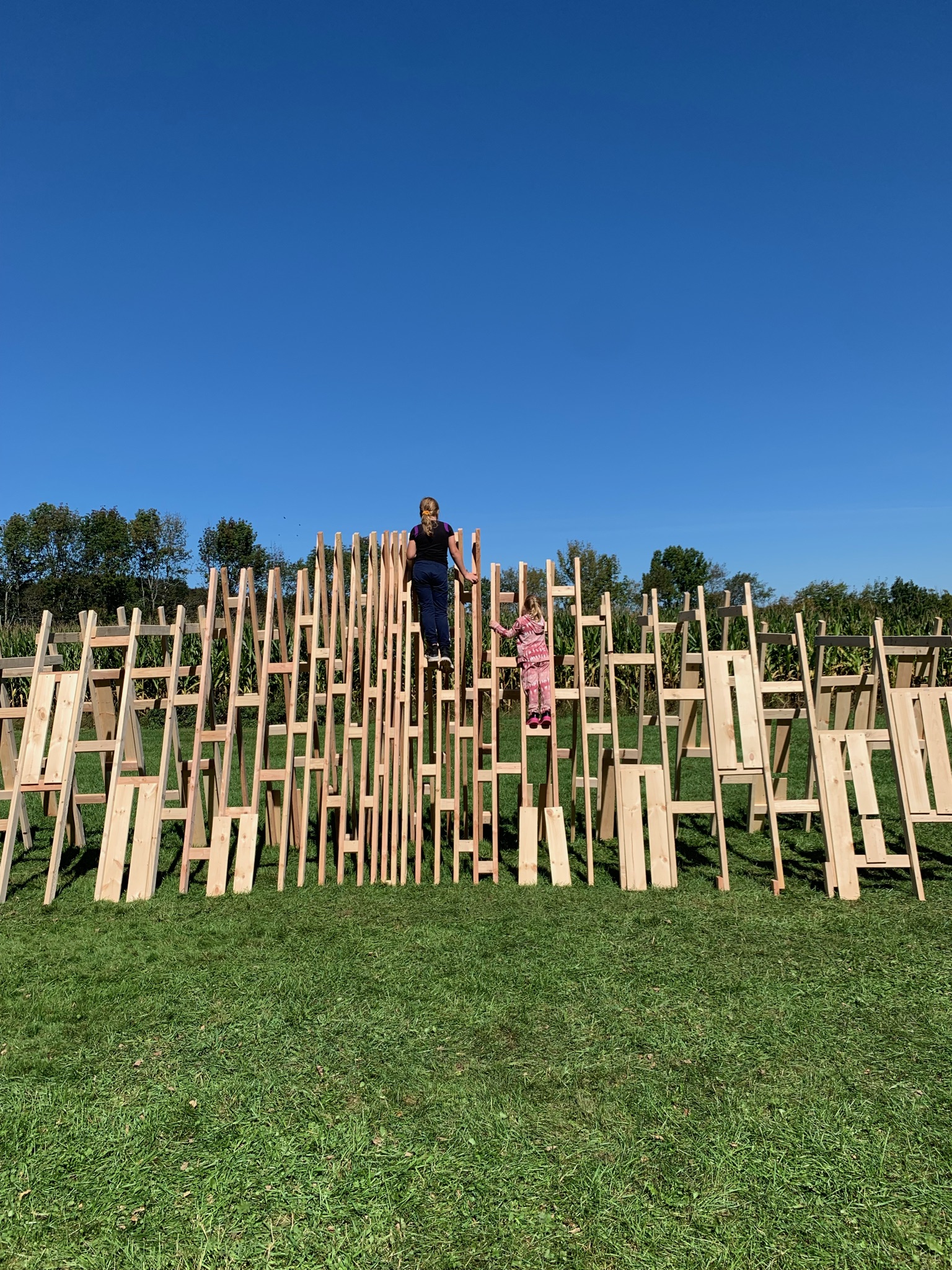 Two people climb a large wooden sculpture.