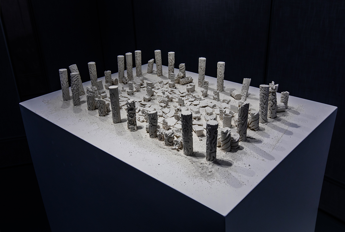 A group of small, cylinder-shaped sculptures stand on a tall surface.