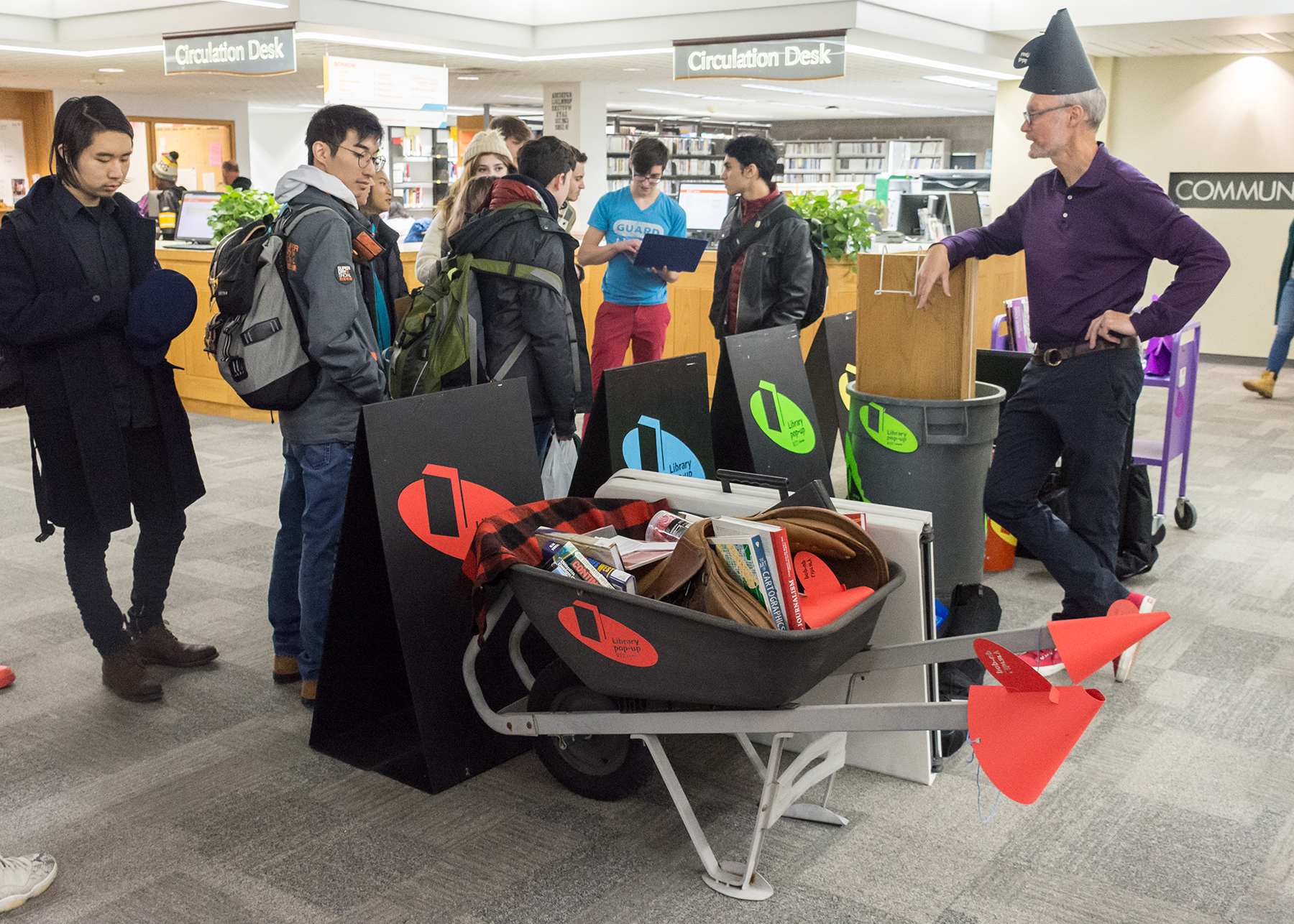 Books and library resources are stuffed in different objects, including a wheelbarrow and garbage tote.