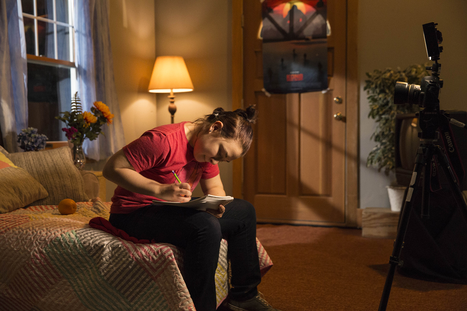 A woman in a red shirt sitting on a couch writing on a pad with a pencil