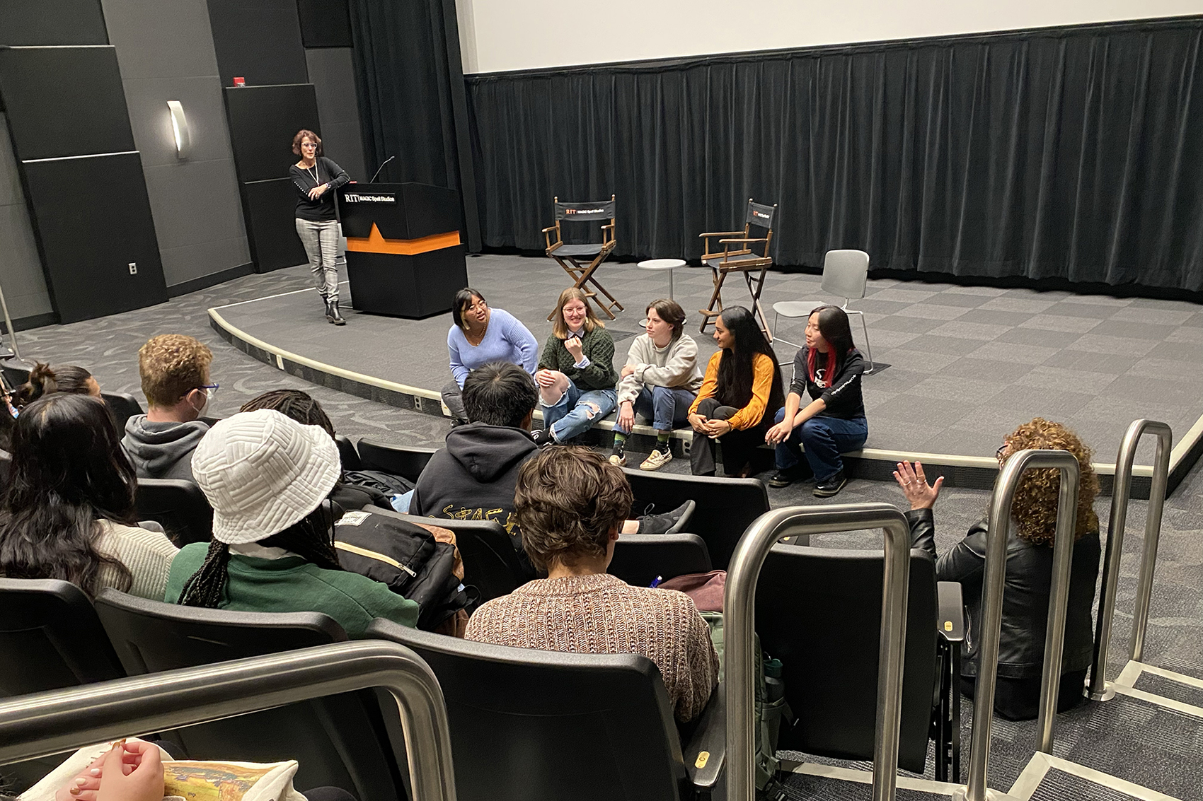 A panel of students speaks to a theater of people.